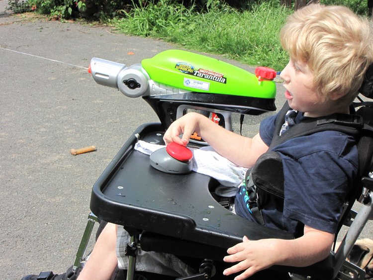 child in a wheelchair using an ability button to shoot a water gun